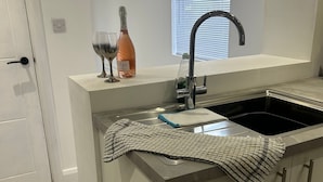 A modern kitchen with a built-in sink, a window with blinds, and a door. - Lakes House Frizington, Cumbria (Cumberland)