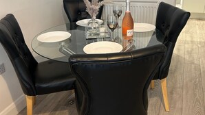A dining table with glass top, black chairs with wooden legs, and a bottle of champagne. - Lakes House Frizington, Cumbria (Cumberland)
