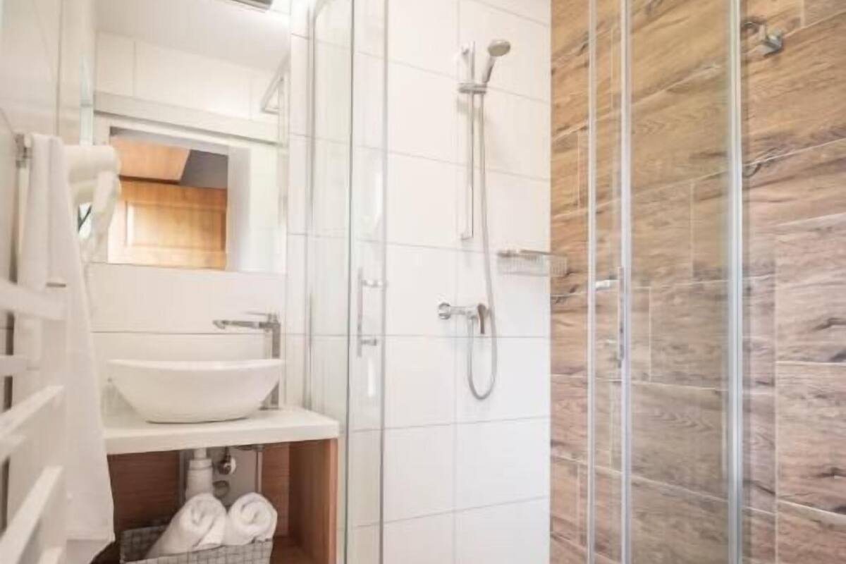 A modern bathroom with a glass shower enclosure, a white sink, and a wooden floor.