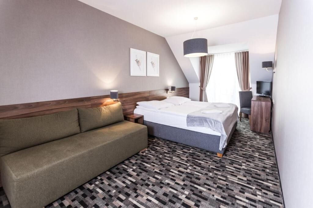 A hotel room with a bed, a sofa, a television, and artwork on the wall.