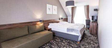 A hotel room with a bed, a sofa, a television, and artwork on the wall.