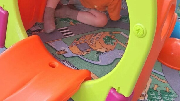 Un enfant dans une structure de jeu colorée, avec un toboggan.