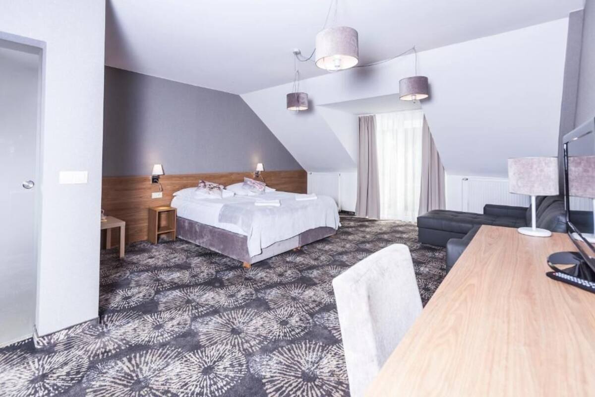 A modern hotel room with a bed, a desk, a sofa, and a TV.