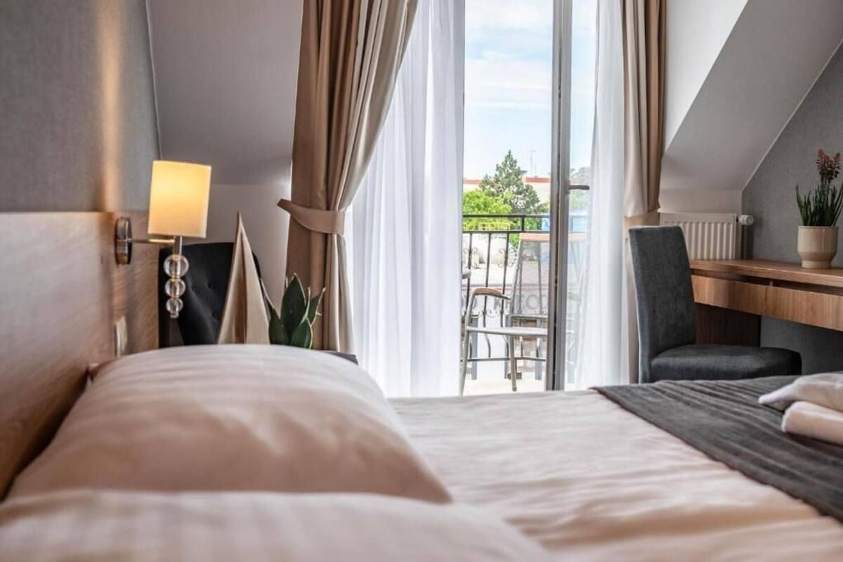 A hotel room with a bed, a desk, a chair, a lamp, and a view of the outside.