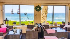 Un salon en bord de mer, doté de meubles en osier, de grandes fenêtres et offrant une vue sur la mer.
