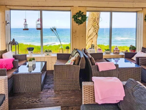 A coastal lounge with wicker furniture, large windows, and a view of the sea.