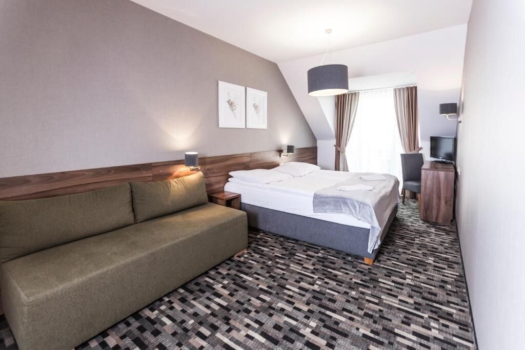 Habitación de hotel con cama, sofá, televisor y escritorio.