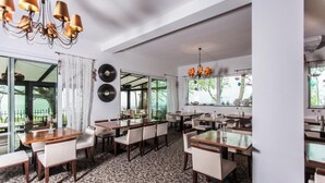 Un restaurant avec un tapis à motifs, des tables en bois, des chaises blanches et un lustre.