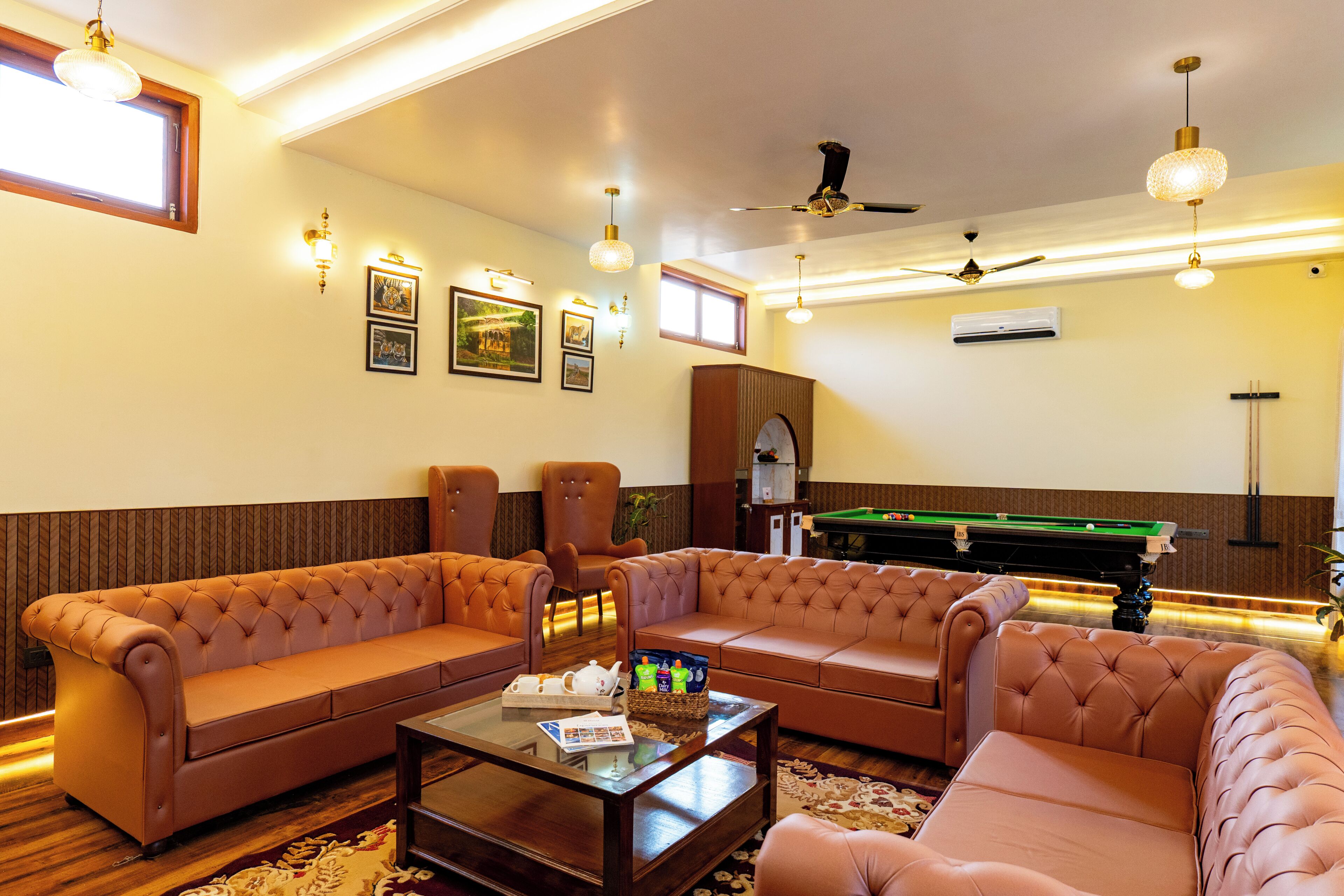 A room with a pool table, two sofas, a coffee table, and wall-mounted lights.