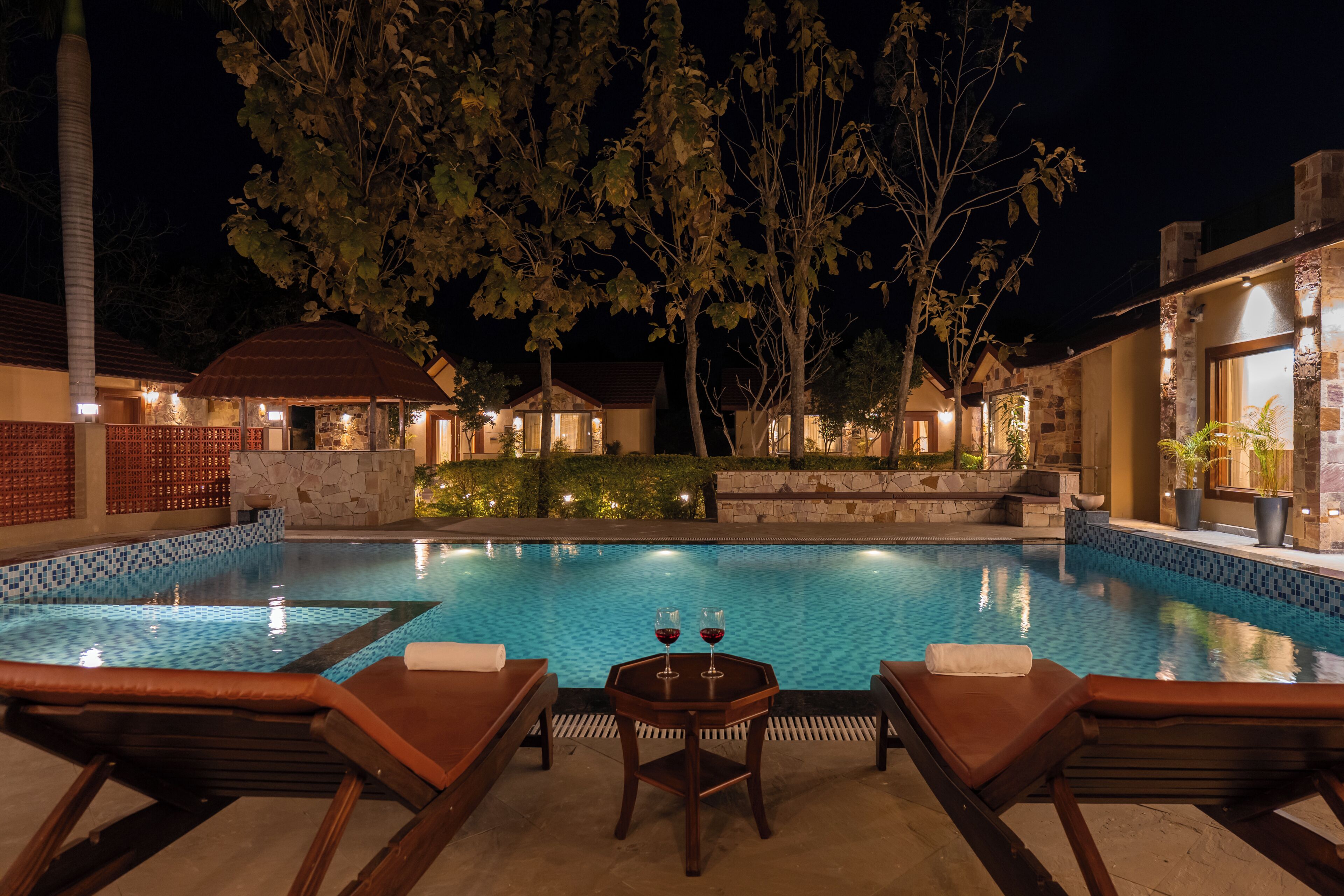 A swimming pool with lounge chairs and a table, surrounded by stone walls and trees.