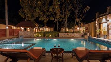 A swimming pool with lounge chairs and a table, surrounded by stone walls and trees.