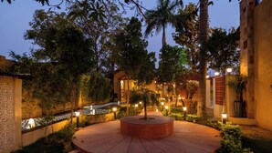 Un espace extérieur circulaire, avec un arbre au centre, entouré d’un petit muret et éclairé par un système d’éclairage d’ambiance.