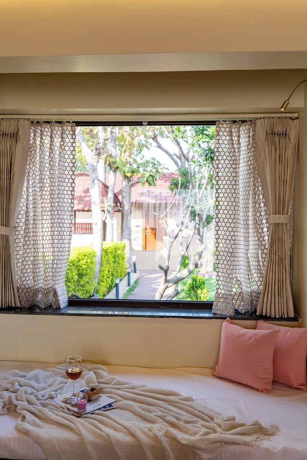 A bed with a blanket, a glass of wine, and a menu on the windowsill. - ELIVAAS Tiger Cave Suite with Pvt Pool (Sawai Madhopur)