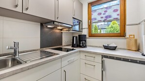 Moderni keittiö, jossa on sisäänrakennettu liesi, kahvinkeitin ja ikkuna, josta avautuu näkymä vehreään maisemaan.