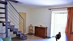 Een moderne woonkamer met een trap, een houten kast, een eettafel met stoelen en een klein houten krukje.