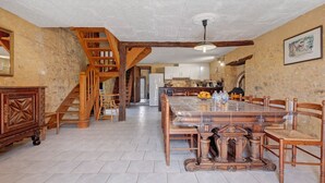 Une cuisine spacieuse avec une grande table à manger, des chaises en bois, un escalier et un mur en pierre.