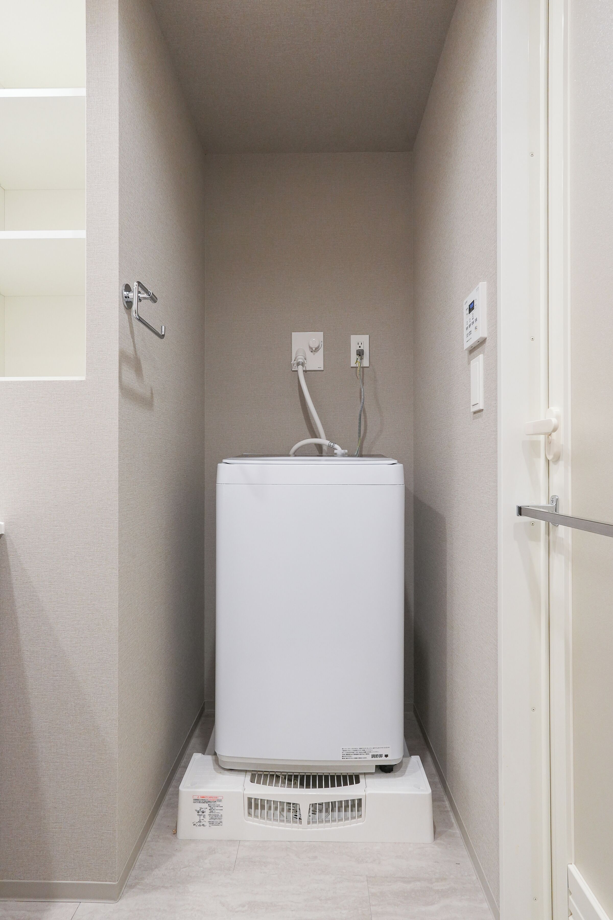 A compact room with a white appliance, possibly a washer, on a stand, a door, and a wall socket.