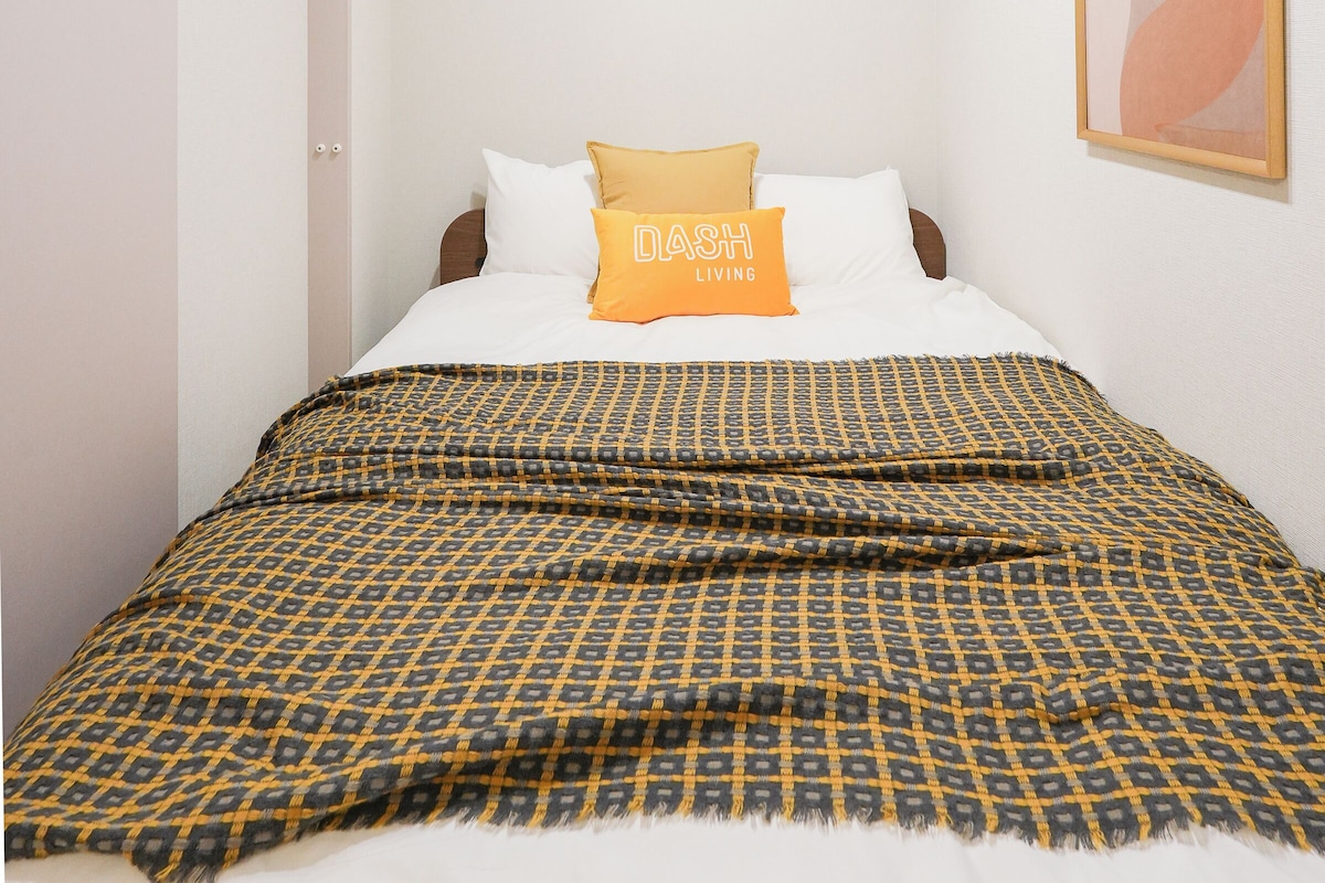 Een slaapkamer met een bed, een plafondlamp en een kunstwerk in een lijst aan de muur.