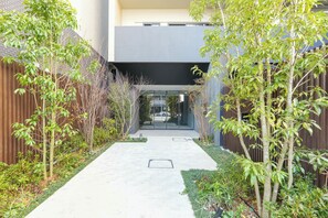 Un étroit chemin de béton bordé de verdure et un bâtiment moderne doté d’un toit plat.