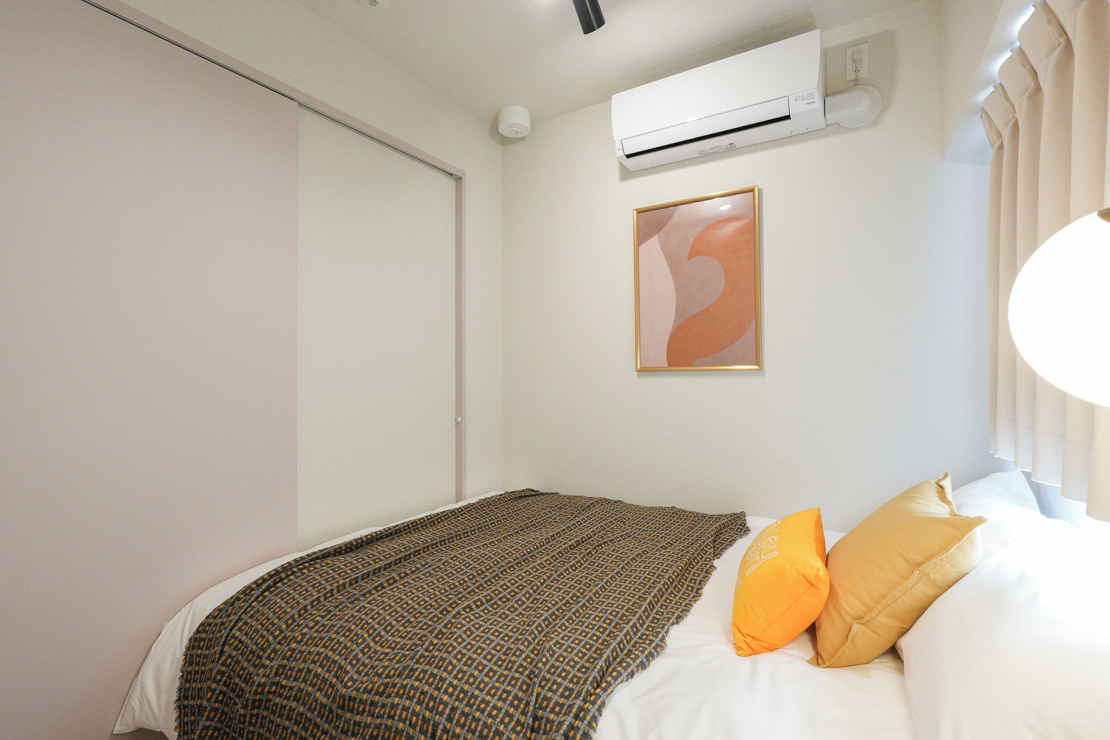 Ein Schlafzimmer mit einem Bett, einer Klimaanlage, einem gerahmten Kunstwerk und einem Fenster mit Vorhängen.