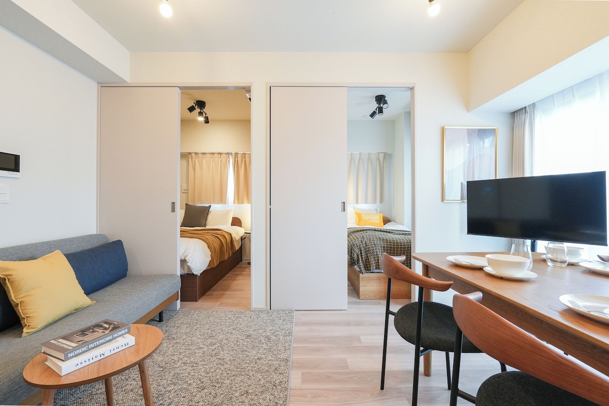 A modern hotel room with a sofa, a dining table with chairs, a TV, and a bed with curtains.