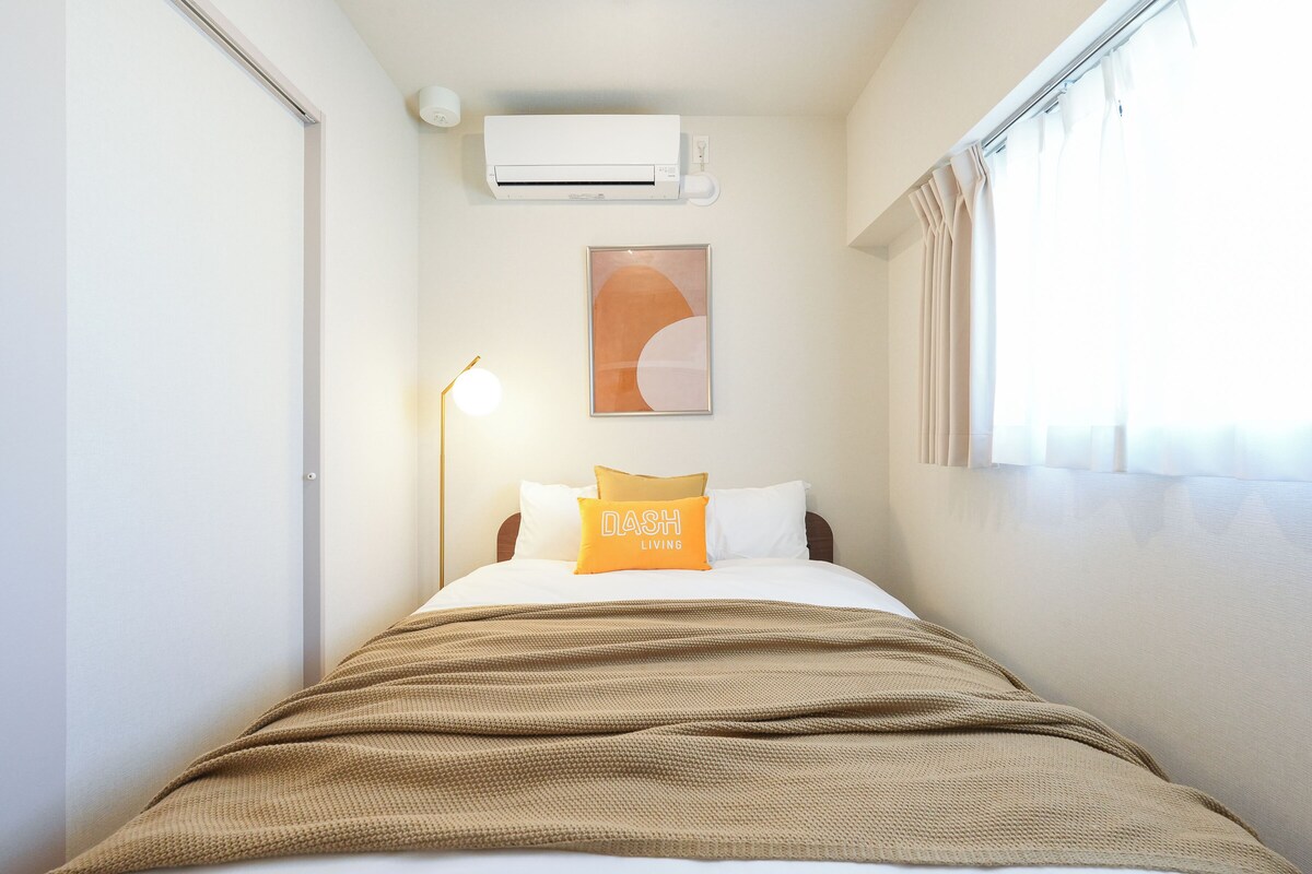 Hotelkamer met een bed, airconditioning, een lijst met kunstwerk, een lamp en een raam met gordijnen.