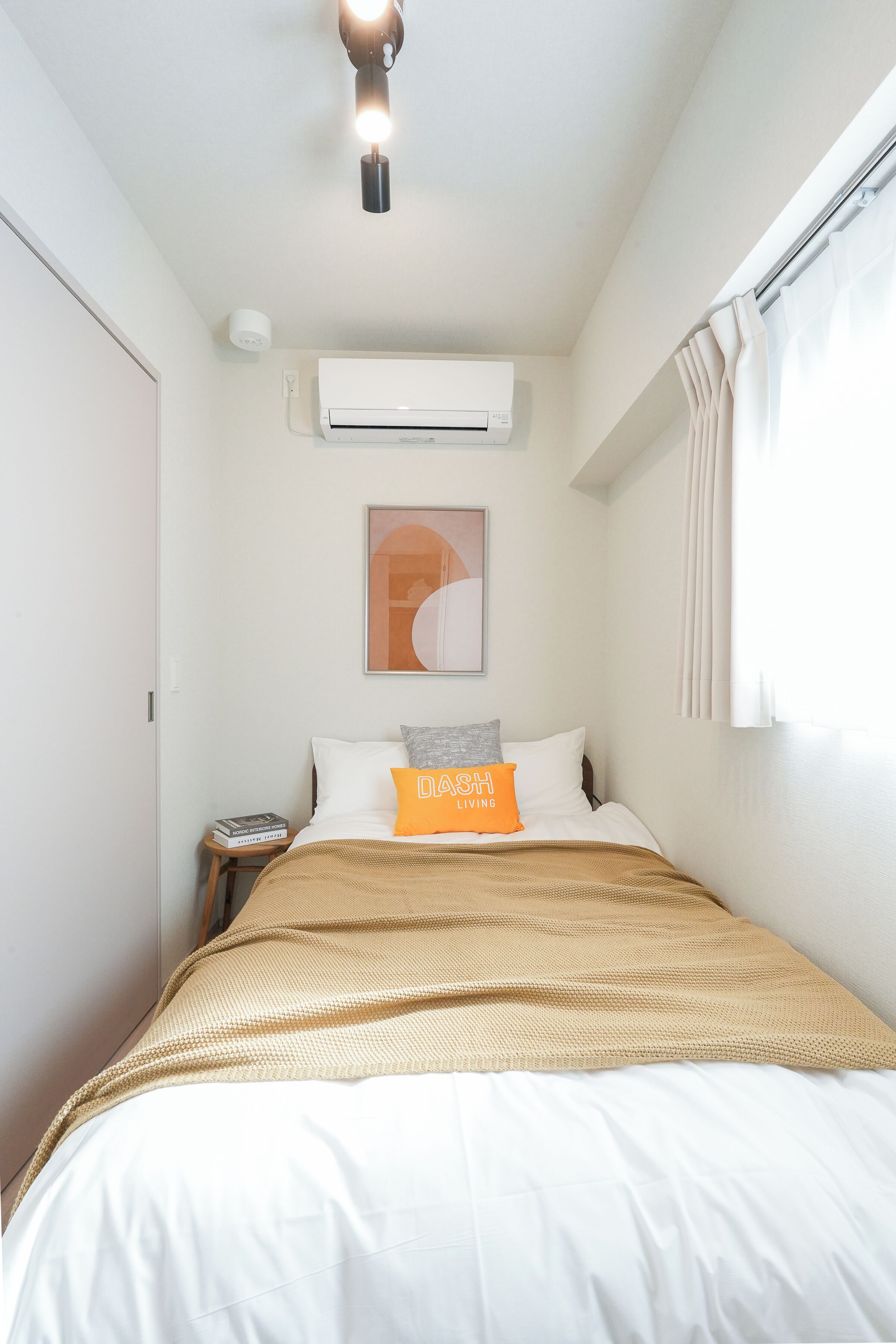 Ein Schlafzimmer mit einem Bett, einer Klimaanlage, einer Deckenleuchte, einem Fenster mit Vorhängen und einem Wandbild.
