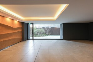 Una habitación amplia con un gran ventanal corredera que da a un espacio exterior, iluminación empotrada en el techo y suelo de baldosas.