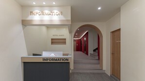 A reception desk labeled 'INFORMATION' with a 'HOTEL AMIGO' sign above it, leading to a staircase. - Hotel Amigo Pyeongtaek Songtan (Pyeongtaek)