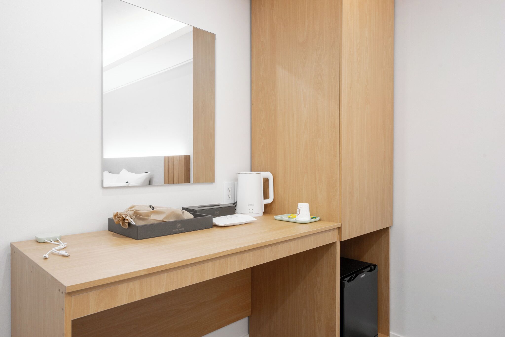 A modern hotel room with a wooden desk, a coffee maker, a kettle, and a trash bin.