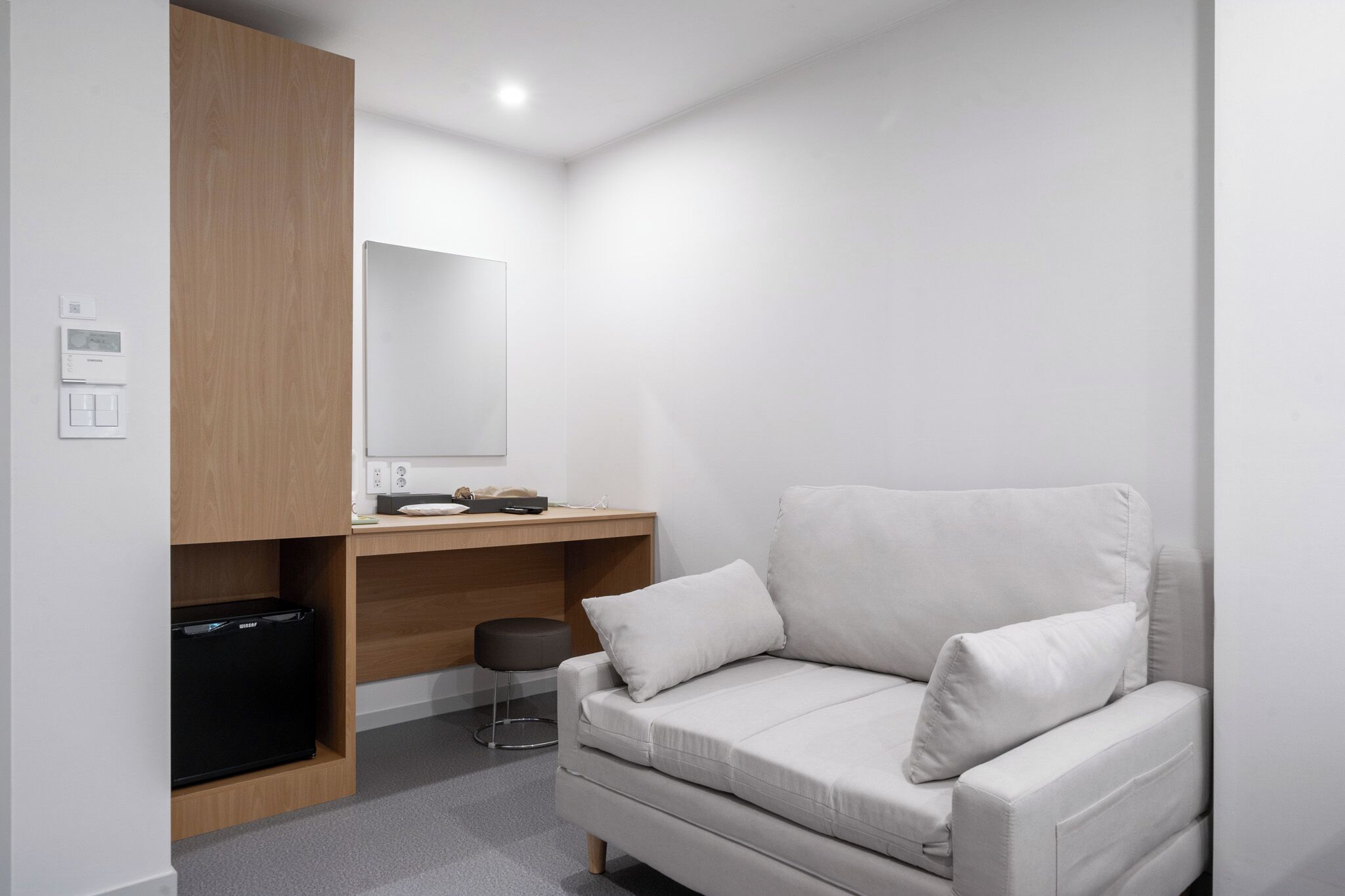 Una habitación moderna con un sofá blanco, un escritorio de madera, un refrigerador negro y un espejo.