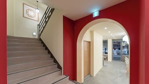A staircase leading to a second floor, a red wall, and an archway leading to a room with a door. - Hotel Amigo Pyeongtaek Songtan (Pyeongtaek)