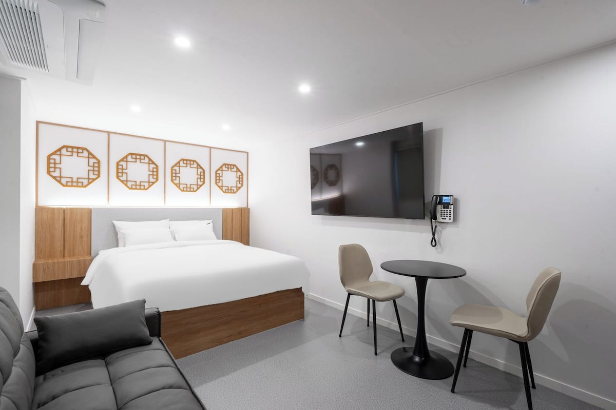 Ein modernes Hotelzimmer mit Bett, Fernseher, Schreibtisch, zwei Stühlen und dekorativen Wandbildern.