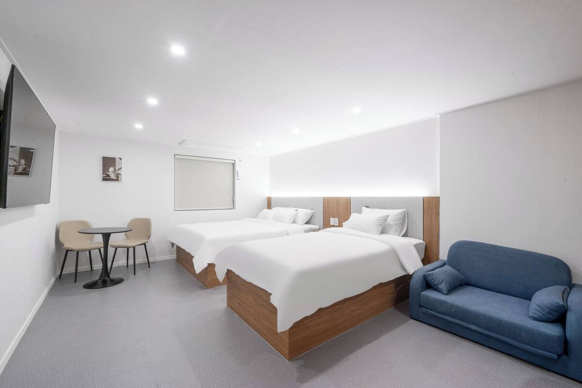 Ein modernes Hotelzimmer mit zwei Betten, einem blauen Sofa, einem kleinen runden Tisch und einer Tafel an der Wand.