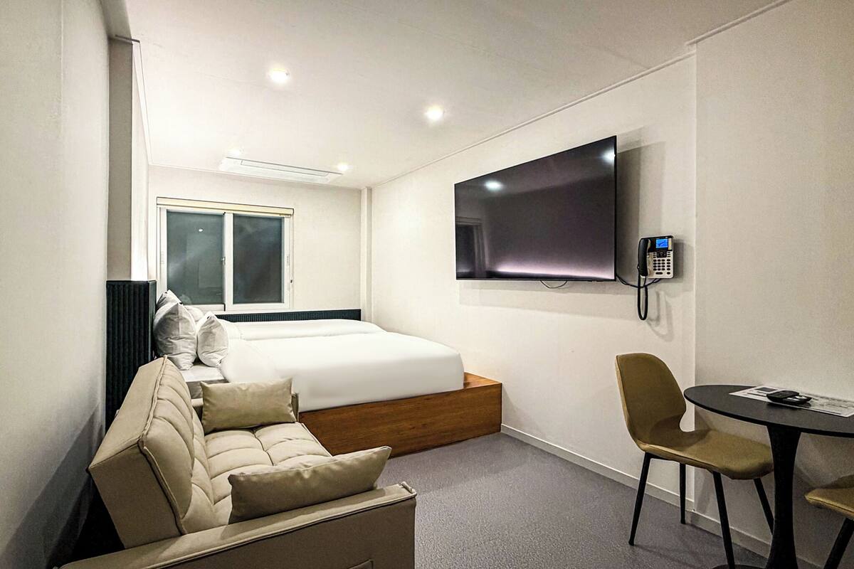 Ein Hotelzimmer mit Bett, Wandfernseher, Schreibtisch mit Stuhl und Fenster.