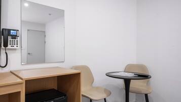 A room with a desk, two chairs, a small table, a black briefcase, a phone, and a mirror.