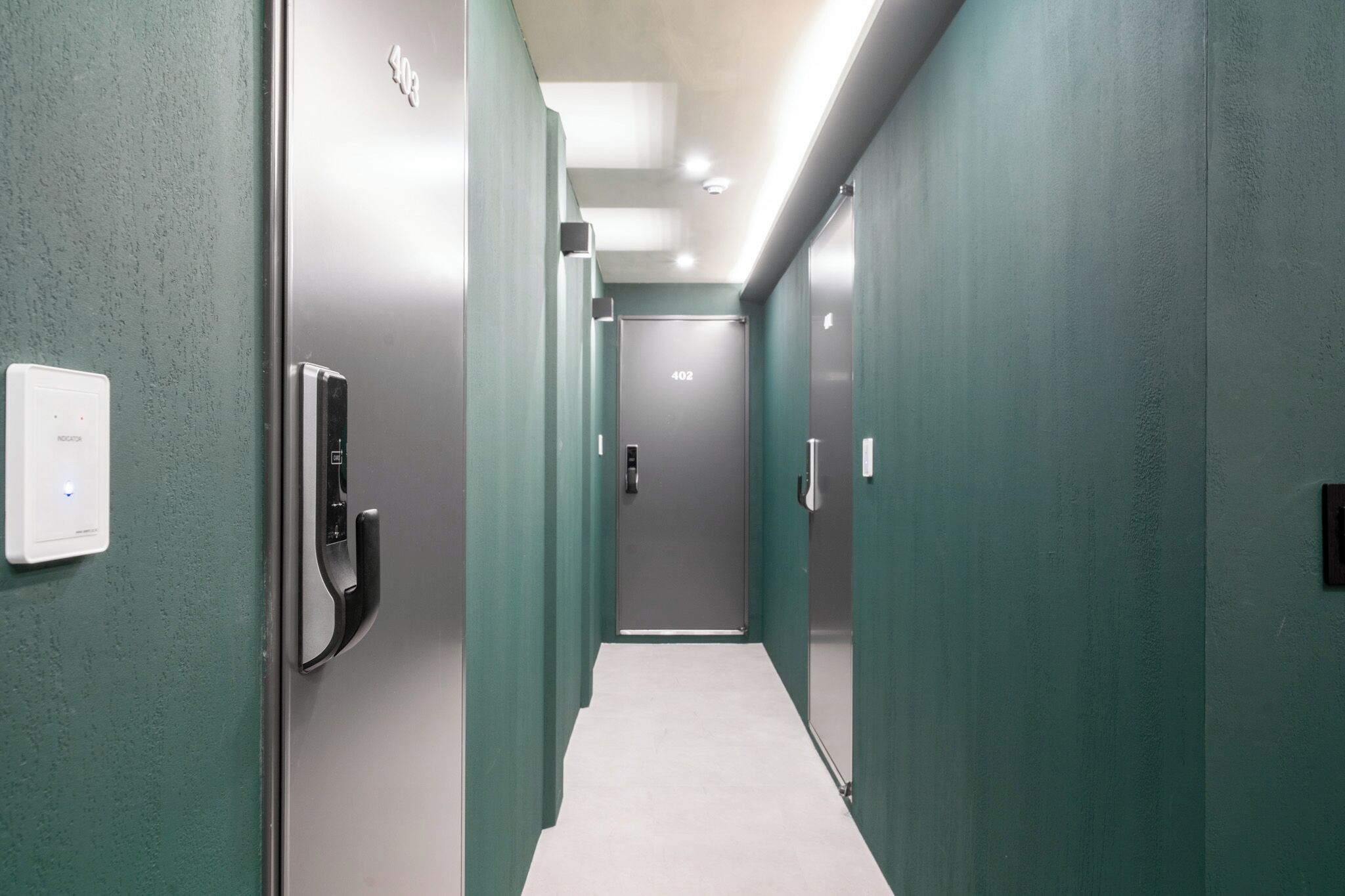Un pasillo con una puerta marcada '402', un portero automático en la pared y un interruptor de luz.