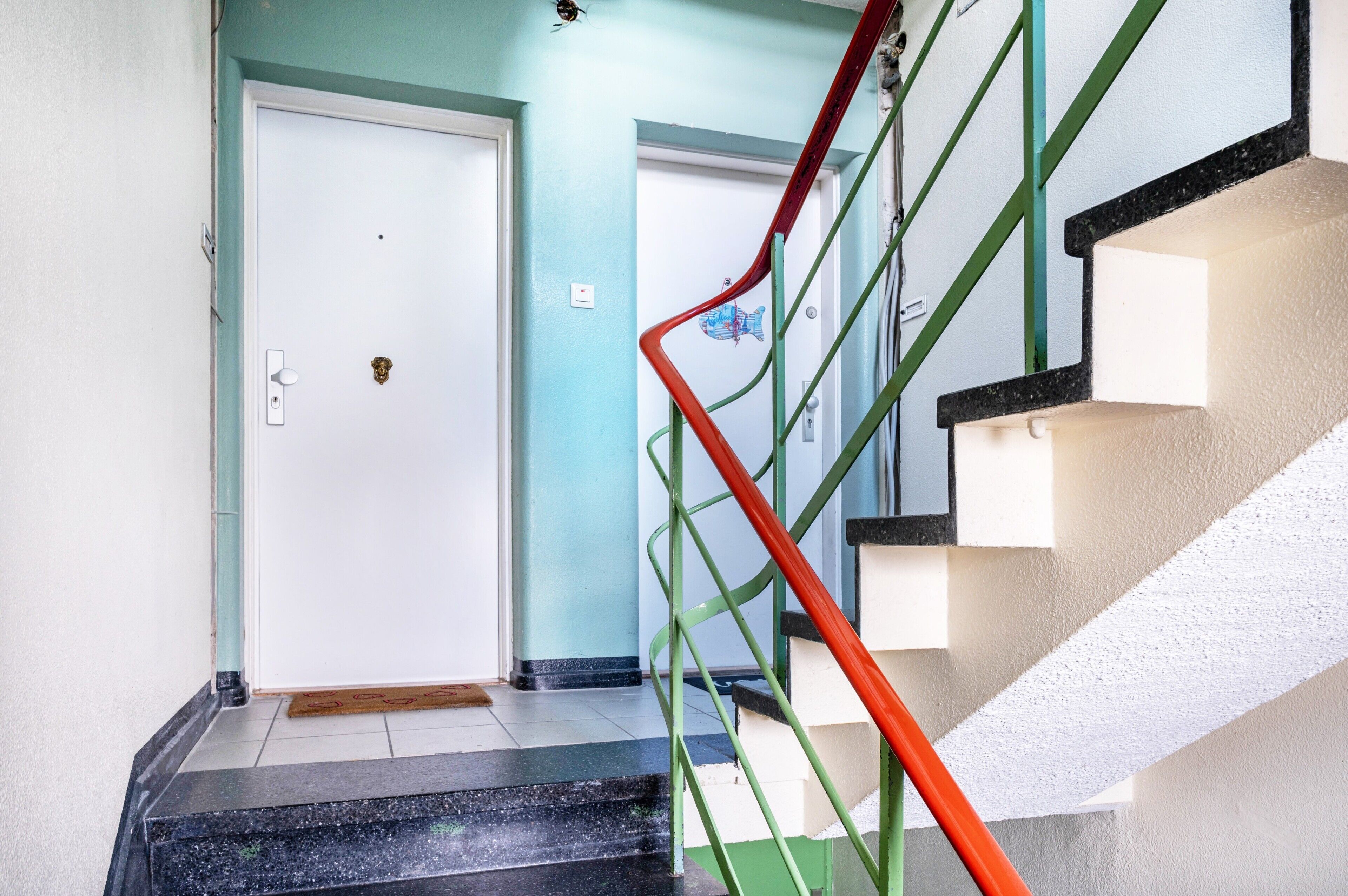 A staircase with green and red railings leading to a white door.