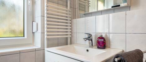 Ein Badezimmer mit einem weißen Waschbecken, einem Spiegel, einem Handtuchhalter und einem Fenster.
