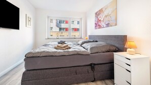 Un dormitorio con cama, lámpara de noche y ventana con vistas a edificios.