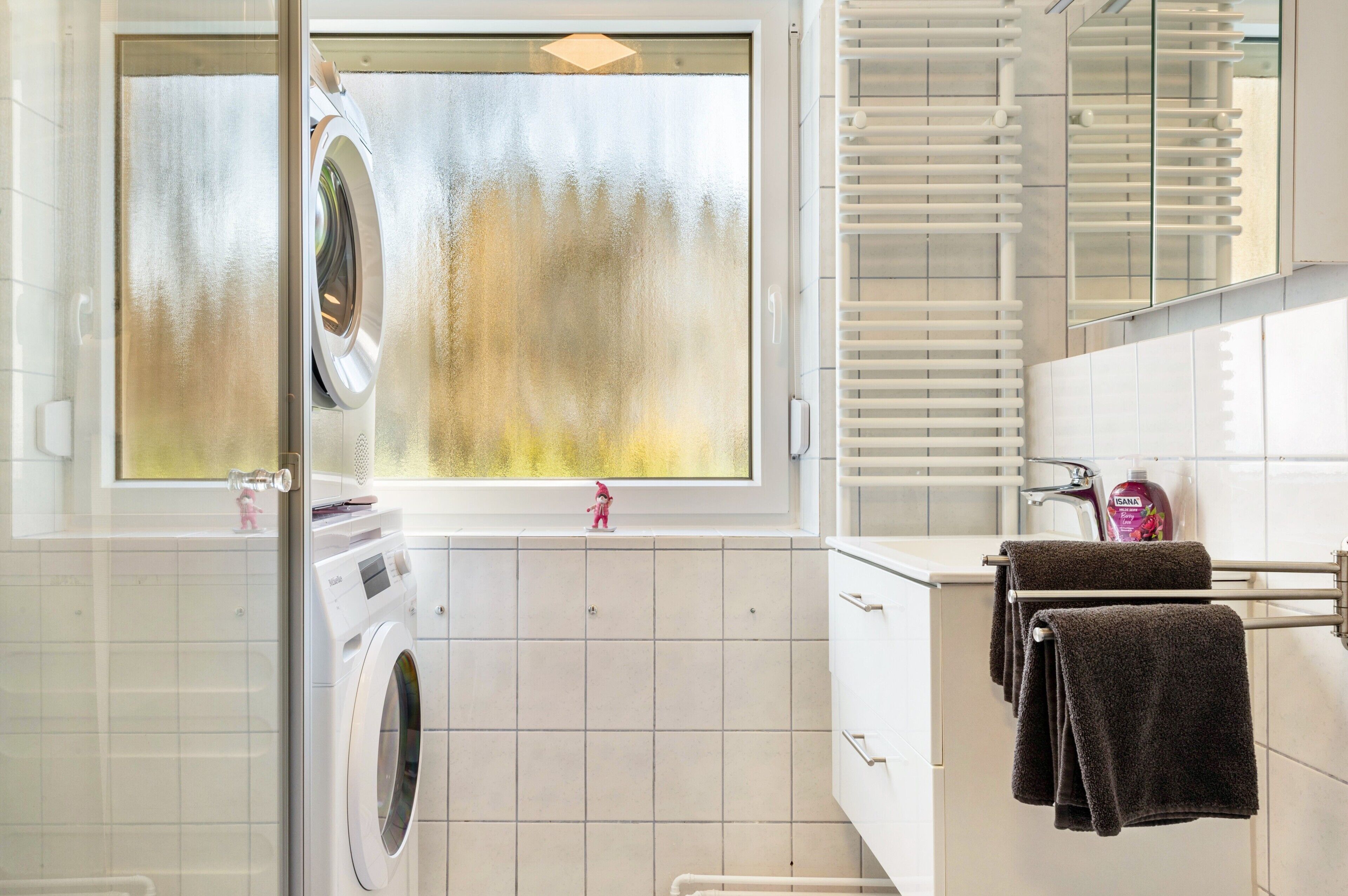 A modern bathroom with a washing machine, a towel rack, and a large mirror.