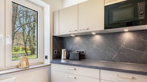 Una cocina con ventana, armarios, microondas y tetera.