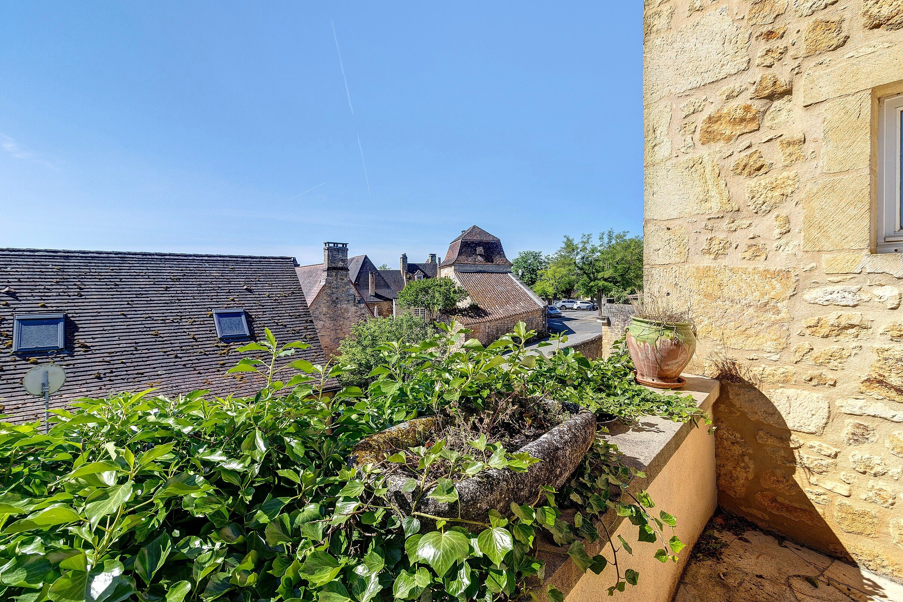 A stone building with a window, a rooftop garden, and a clear blue sky.
