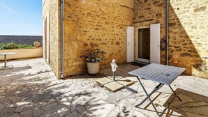 Un patio de piedra con una mesa, sillas, una planta en maceta y una puerta que da a un edificio.