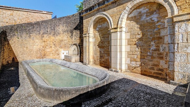 Un área de baño con piedra, que incluye una piscina rectangular, arcos y una pared de piedra.