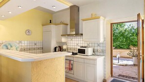 Una cocina con armarios blancos, un microondas y un ventanal amplio.