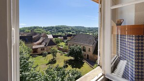Vista dalla finestra su un cortile con edifici tradizionali, cielo sereno e una collina in lontananza.