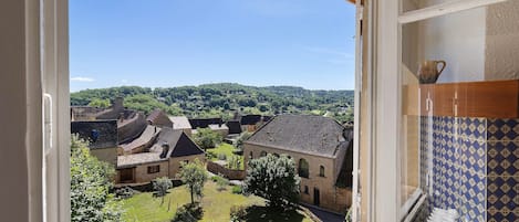 A view from a window overlooking a courtyard with traditional buildings, a clear sky, and a distant hill.