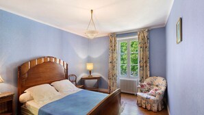 Una camera da letto con un letto in legno, un comodino, una sedia, una finestra con tende e un termosifone.
