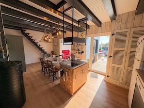 A kitchen with a wooden island, a dining area with chairs, a staircase, and a view through a glass door to an outdoor patio. - L'escale - A cosy little retreat for four, close to the sea (Plougonvelin)